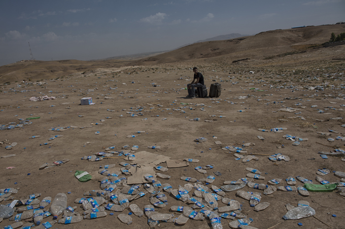 A man waits among water bottles, near the Sahela border point in Dohuk, northern Iraq. Photo by Lynsey Addario, August 21, 2013.