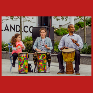Three people seated playing hand drums. 