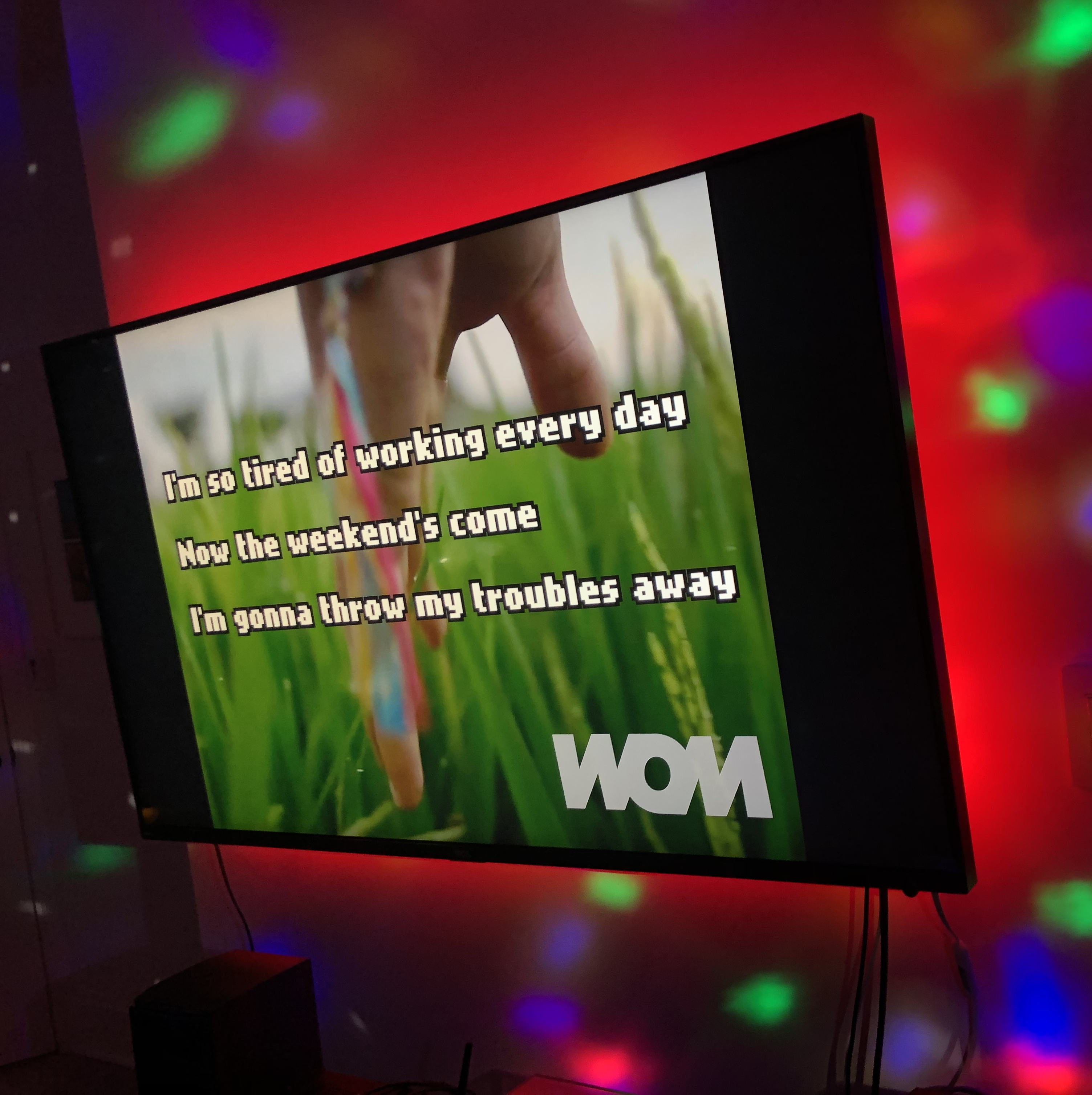 A TV screen with song lyrics, in a room with multicolored lighting.