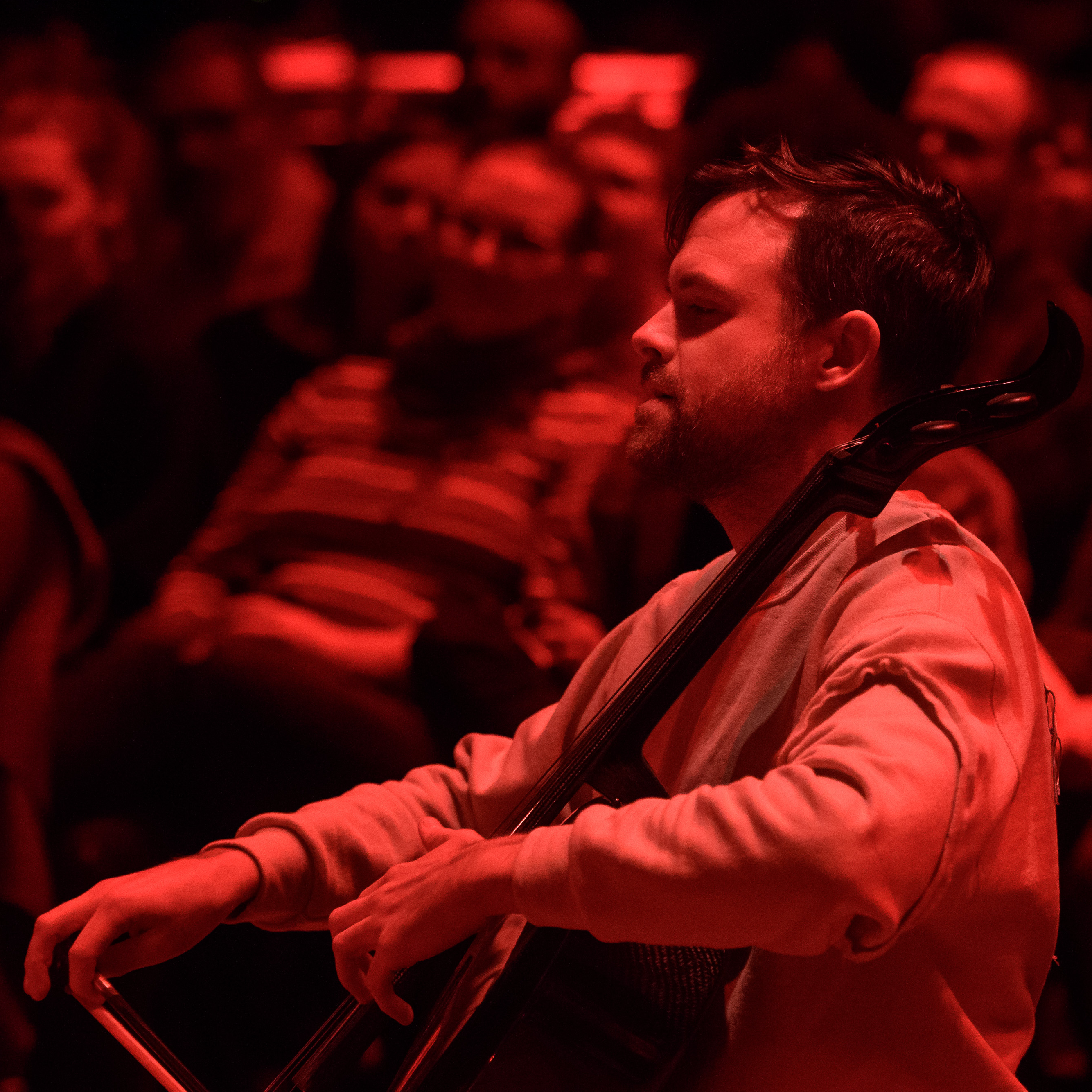 Photograph with a red tint of Ethan Philbrick playing a cello.