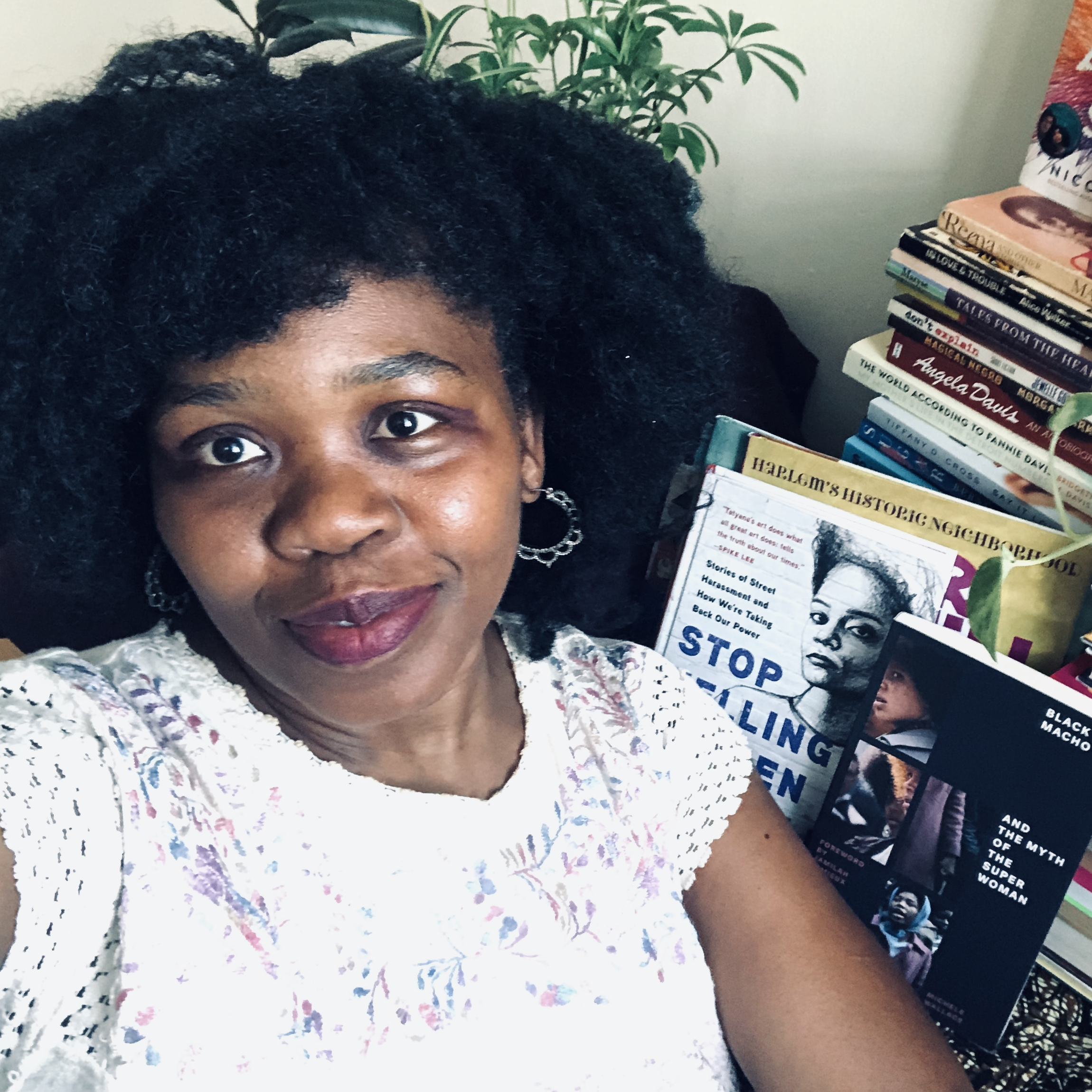 A woman with dark skin, a white shirt, in front of a set of books.