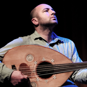 A man against a black background holding a string instrument.
